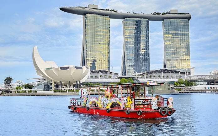 Singapore River Cruise boat with colorful designs in front of Marina Bay Sands.