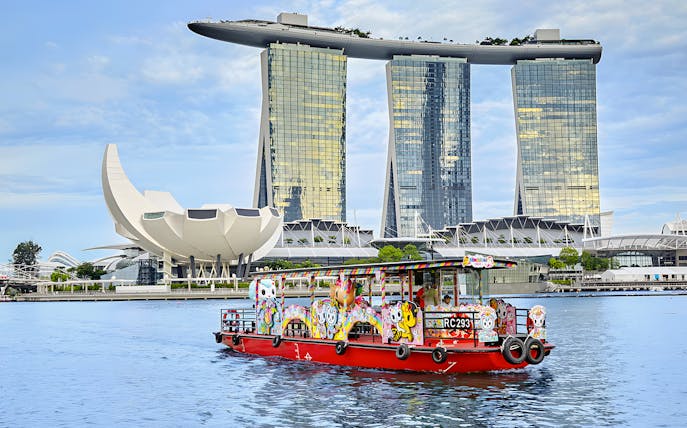 Singapore River Cruise boat with colorful designs in front of Marina Bay Sands.