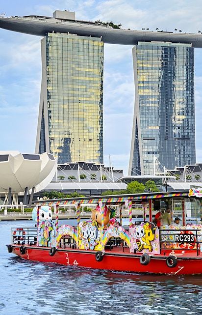 Singapore River Cruise boat with colorful designs in front of Marina Bay Sands.