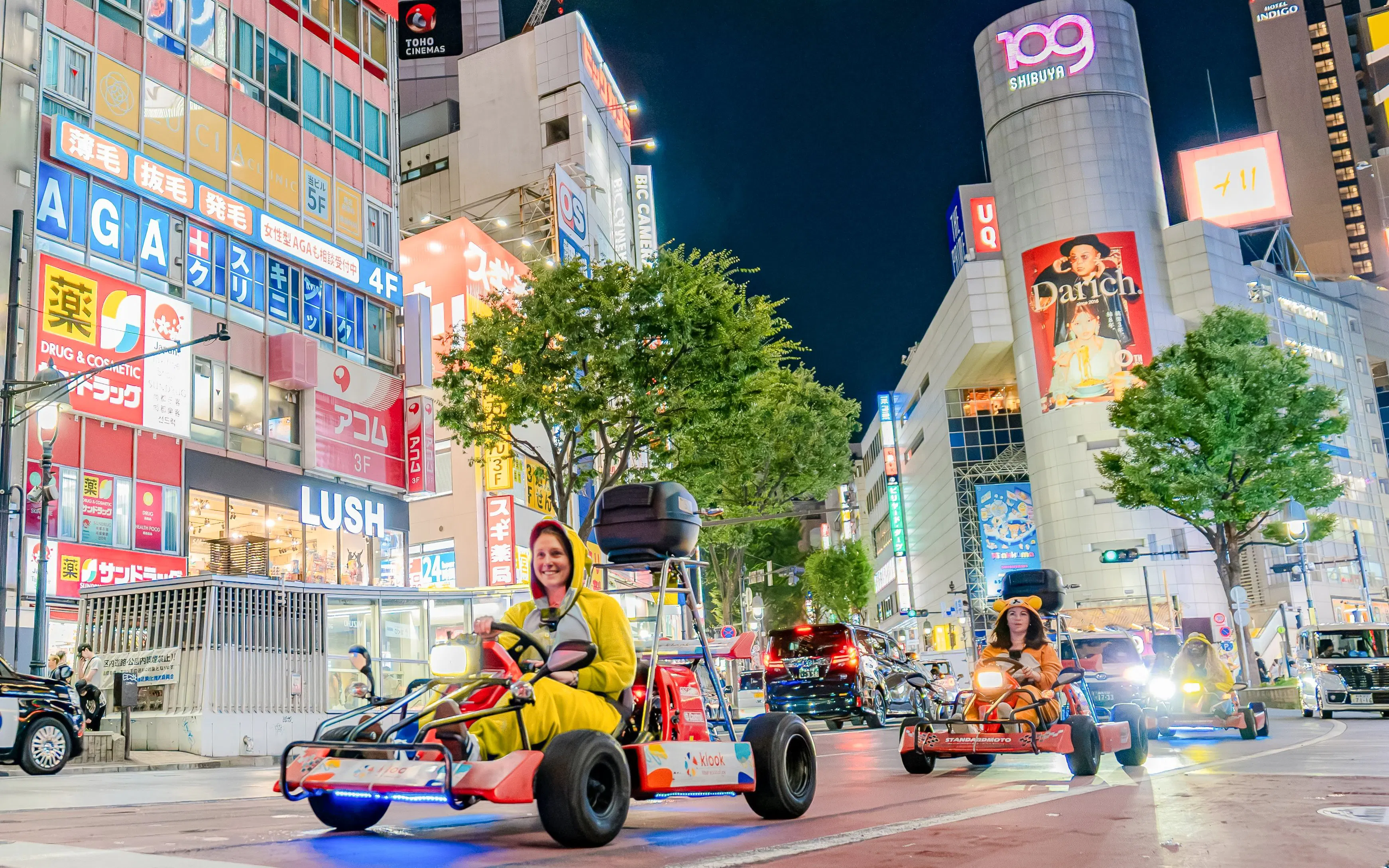 Tourists in costumes driving go-karts through Shibuya, Tokyo at night.