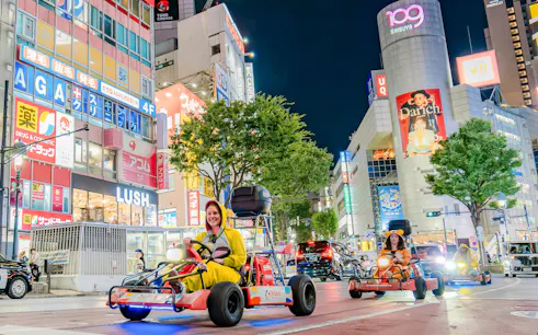 Tourists in costumes driving go-karts through Shibuya, Tokyo at night.