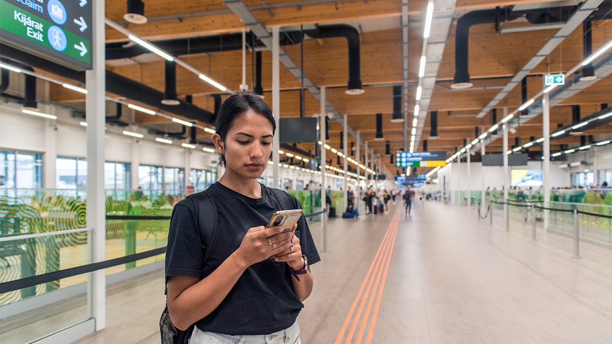 Traveler using phone at Budapest Airport terminal.