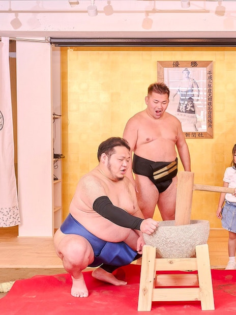 Tourists pounding mochi with a retired sumo wrestler at Ryogoku, Tokyo.