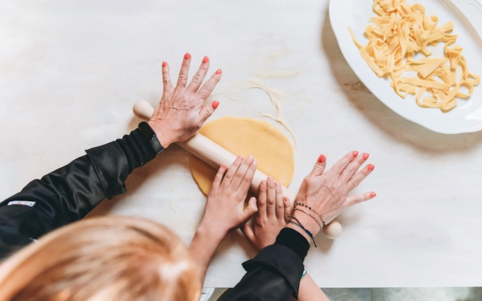 Hands rolling fresh pasta dough in a cooking class.