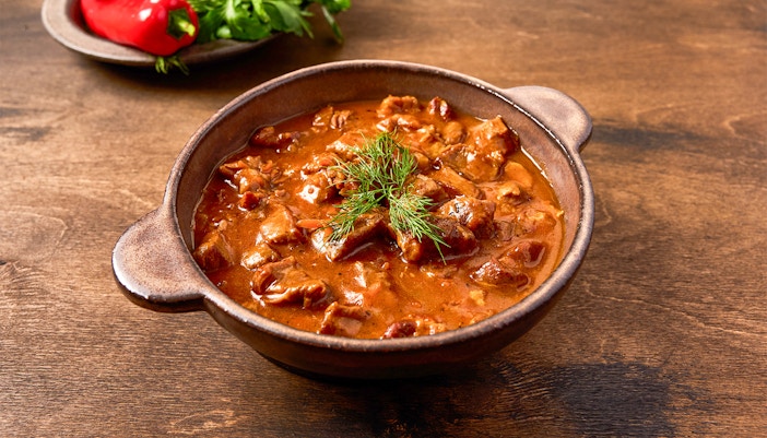 Hearty beef stew in a rustic bowl with fresh herbs, part of a foodie bucket list experience.
