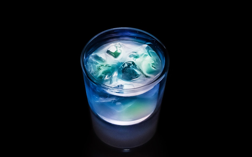 Iced tea with glowing blue and green hues in a glass, representing dynamic equilibrium.