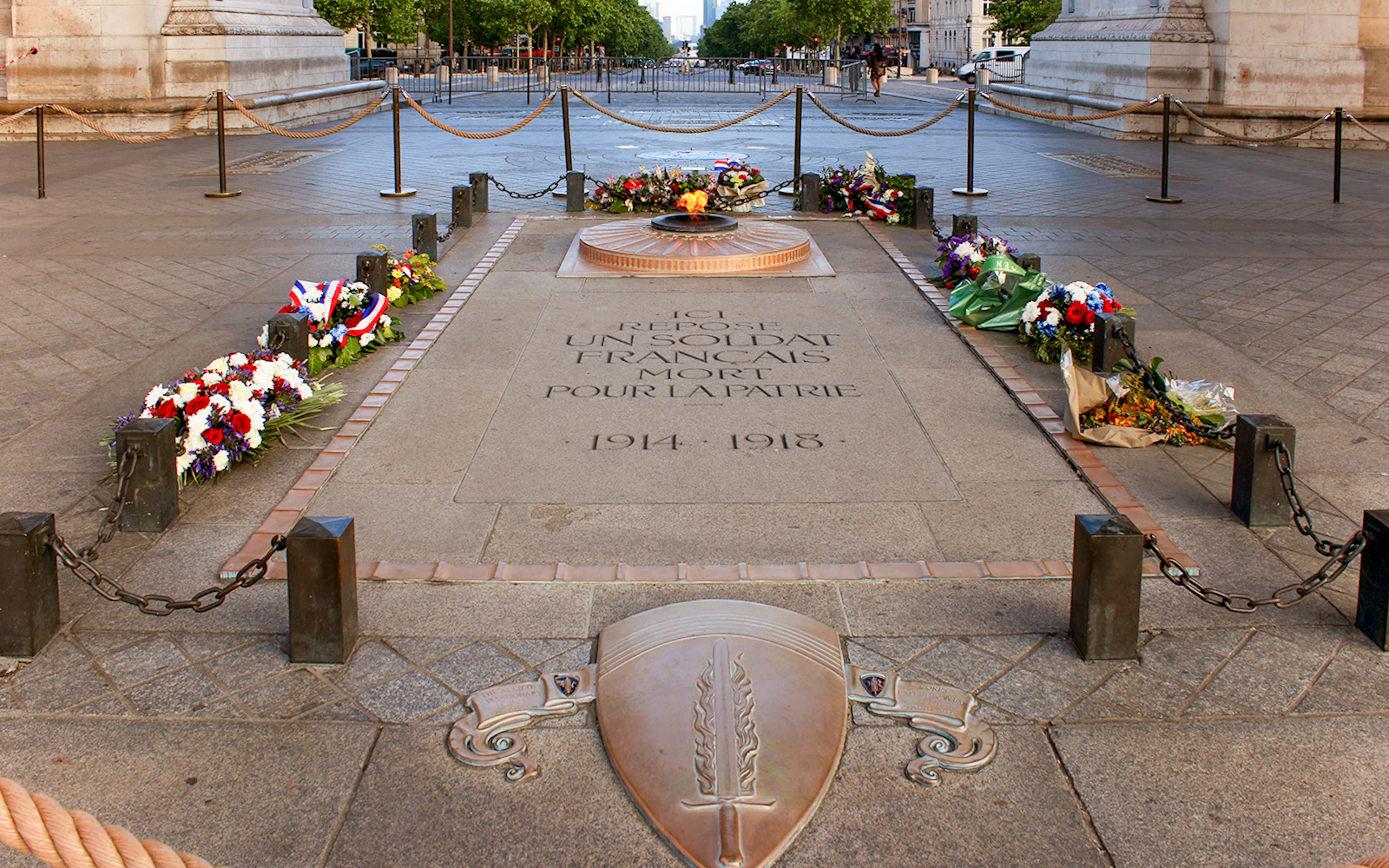 Unknown soldier's grave with eternal flame at Arc de Triomphe, Paris, surrounded by flowers.
