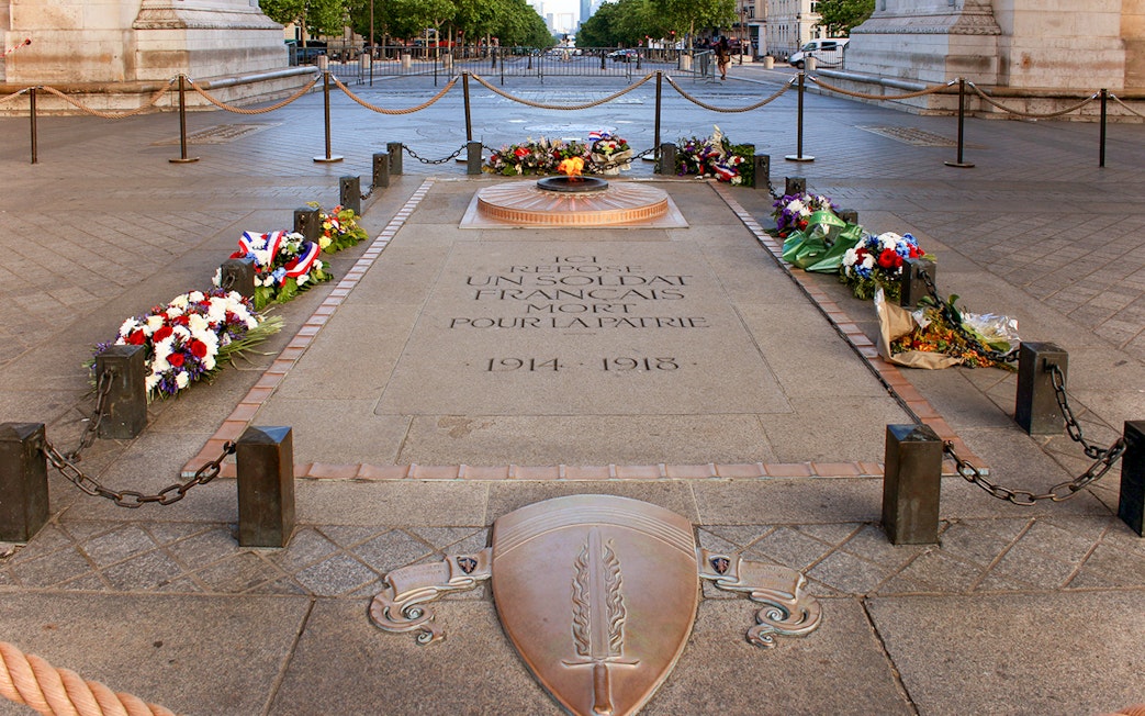 Unknown soldier's grave with eternal flame at Arc de Triomphe, Paris, surrounded by flowers.