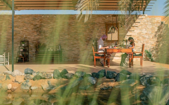 Couple enjoying breakfast at an outdoor table with stone wall backdrop.