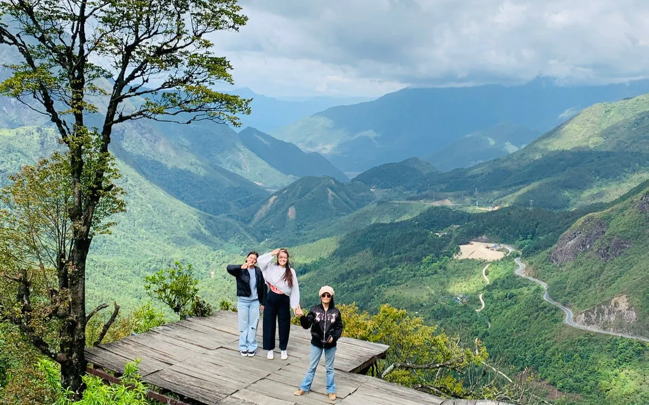 Tourists on a wooden platform overlooking Sapa's lush green mountains and winding roads.