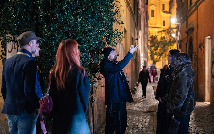 Local guide leading a haunted ghost tour in a narrow street in Rome at night.