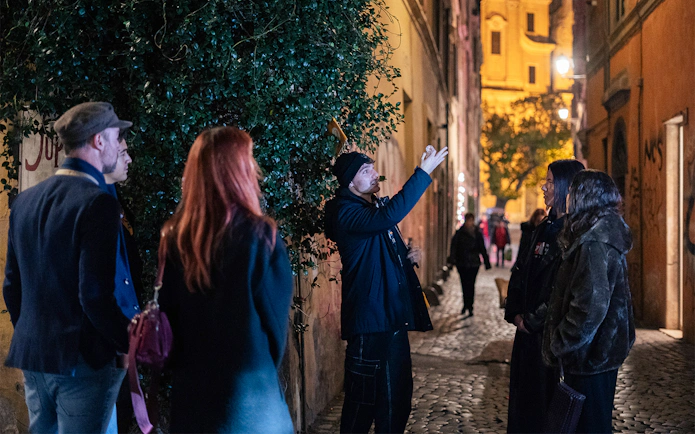 Local guide leading a haunted ghost tour in a narrow street in Rome at night.