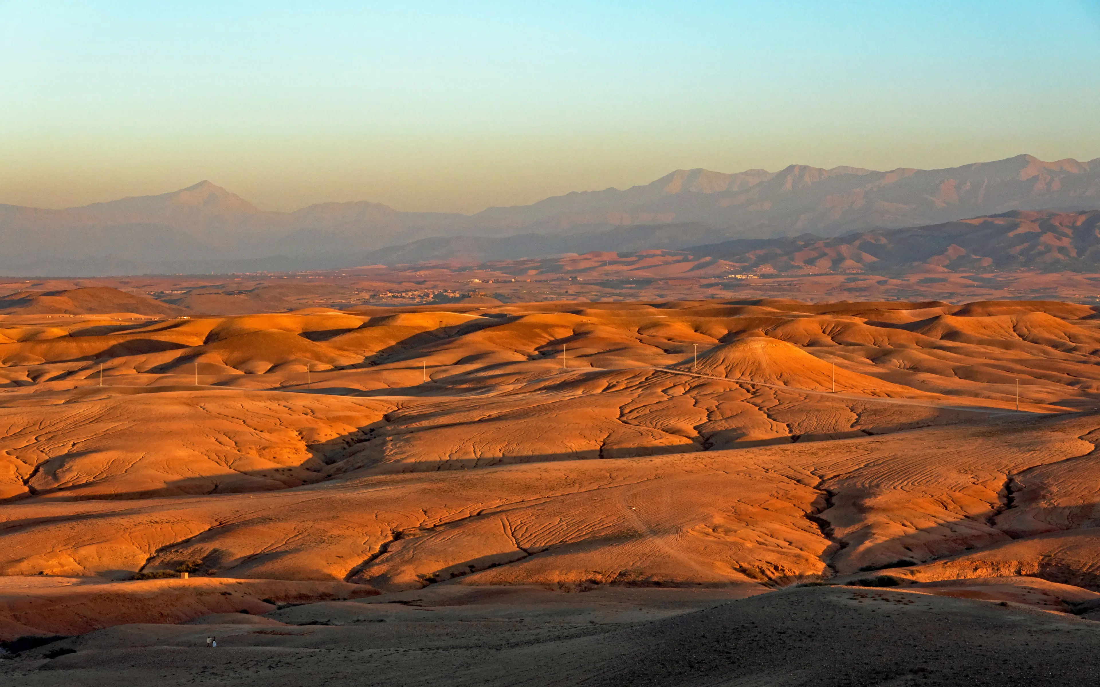 Sunset over rolling dunes in Agafay Desert, Morocco with distant mountains.