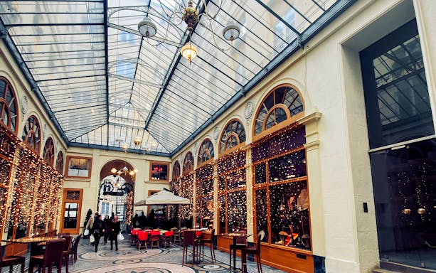 Covered passage in Paris with glass roof, arched windows, and people walking.