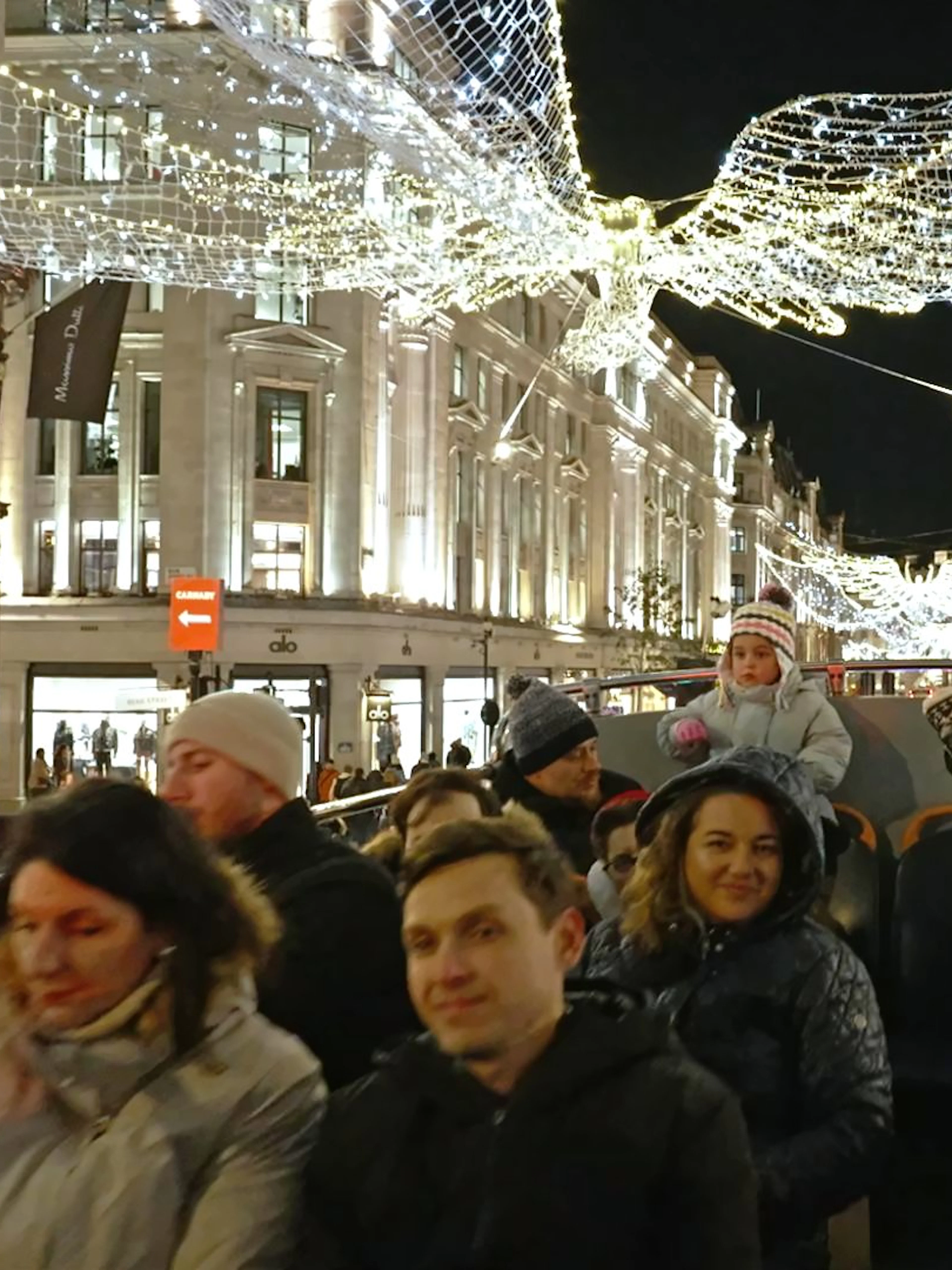 Open-top bus tour of London's Christmas lights on Regent Street at night.