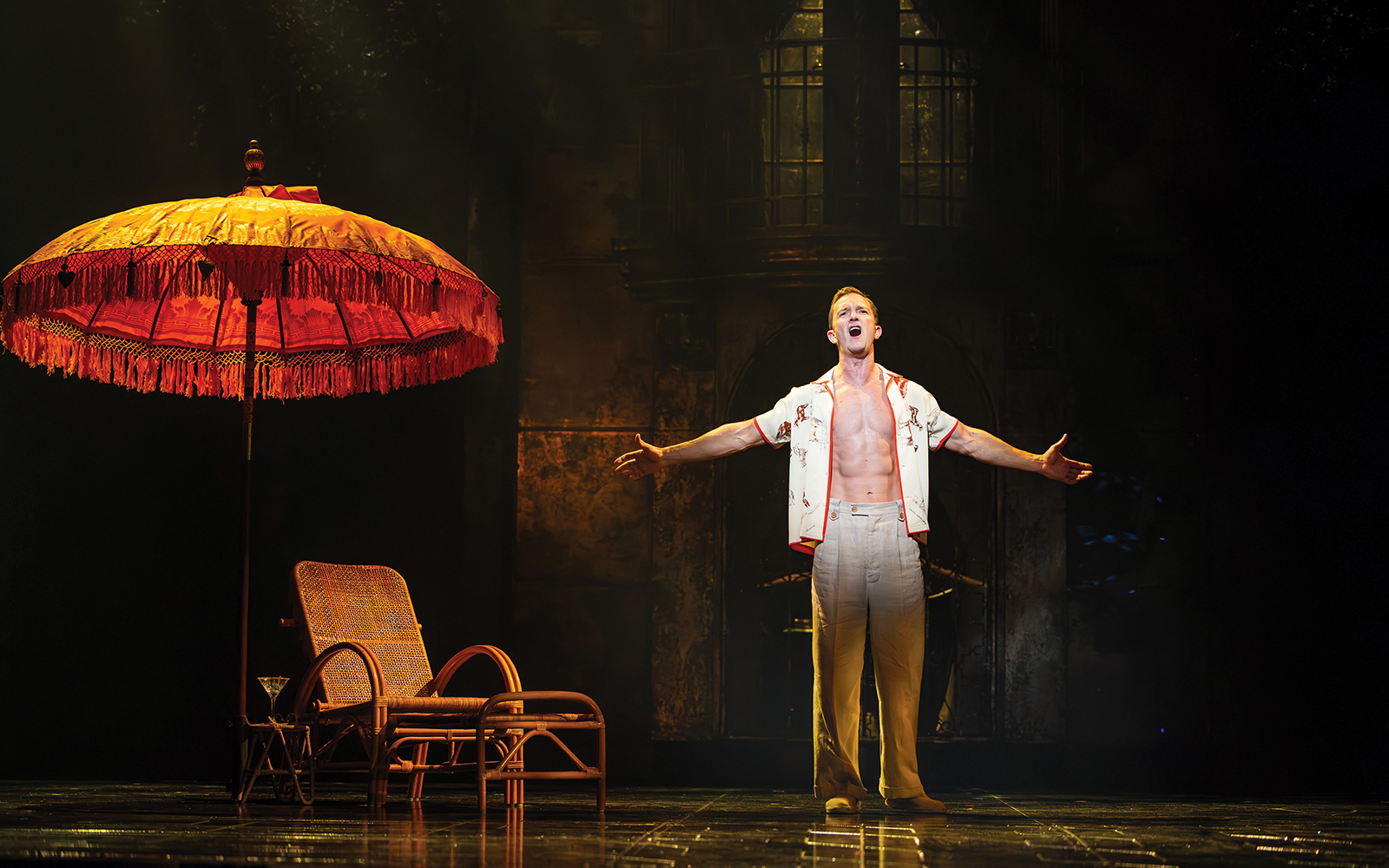 Performer singing under a large umbrella on stage, Sunset Boulevard.