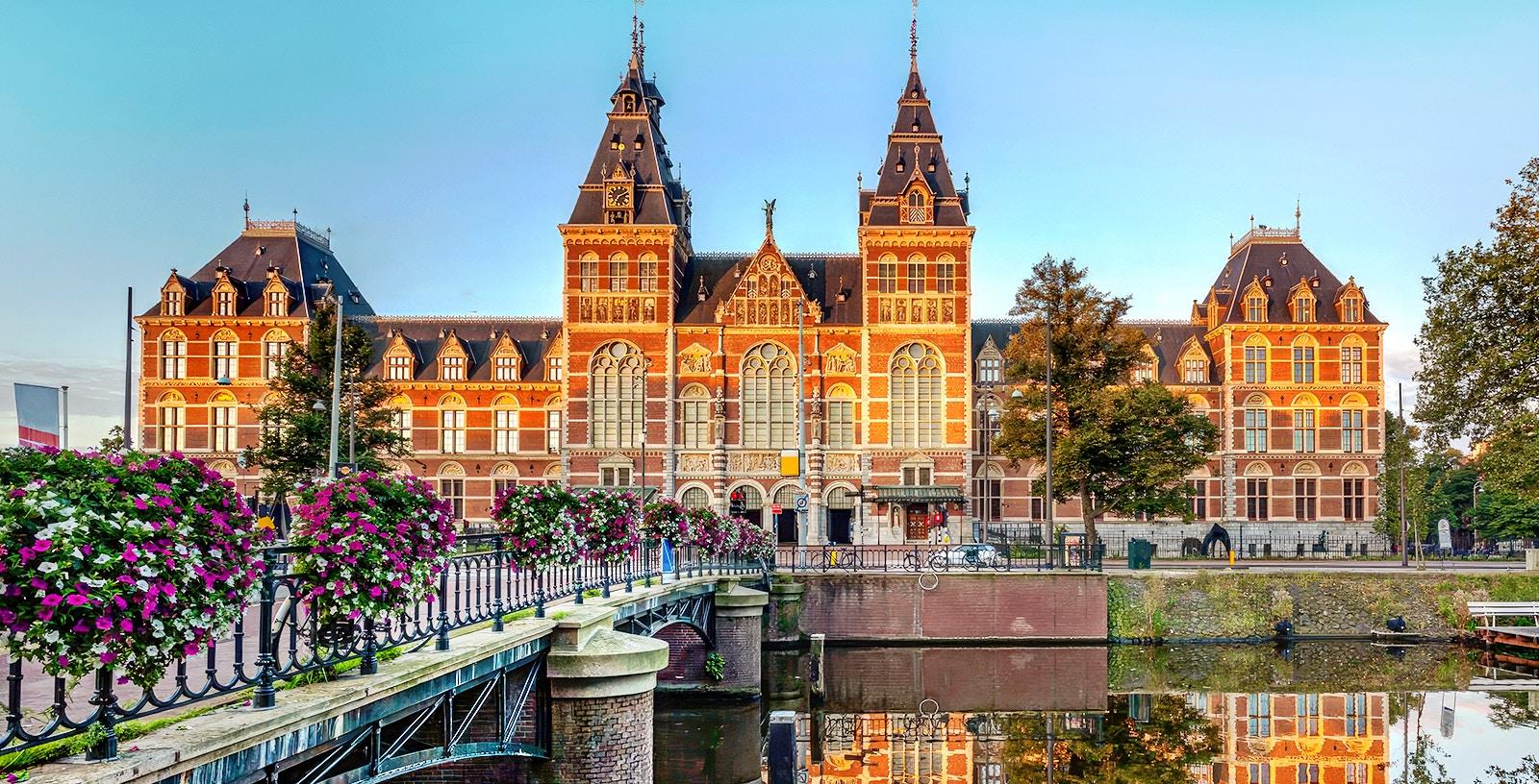 Rijksmuseum exterior with canal and flower-lined bridge in Amsterdam.