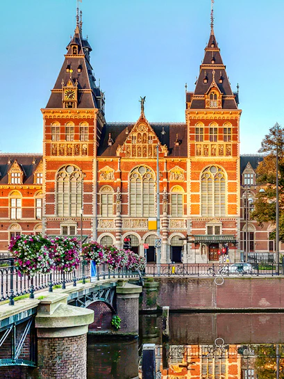 Rijksmuseum exterior with canal and flower-lined bridge in Amsterdam.