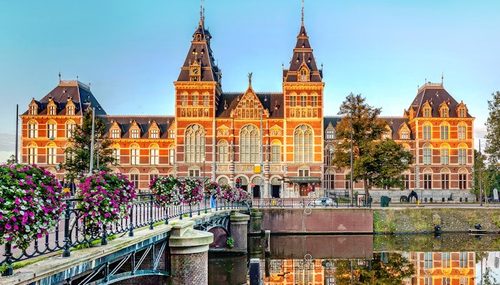 Rijksmuseum exterior with canal and flower-lined bridge in Amsterdam.