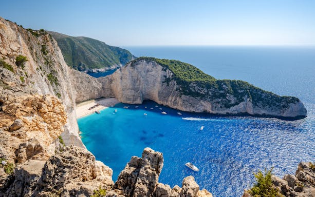 Navagio Beach and cliffs with boats in Zakynthos, Greece, viewed from above.
