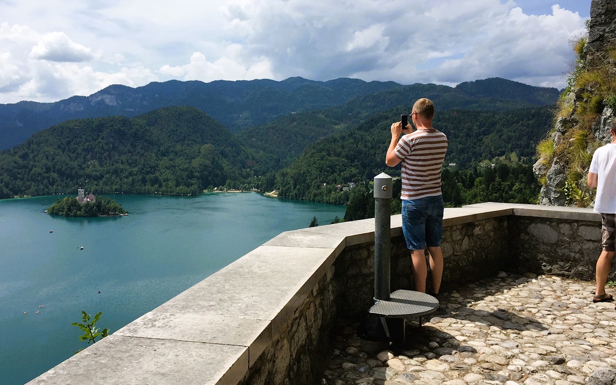 Tourist photographing Lake Bled from a viewpoint, featuring the island church, Slovenia.