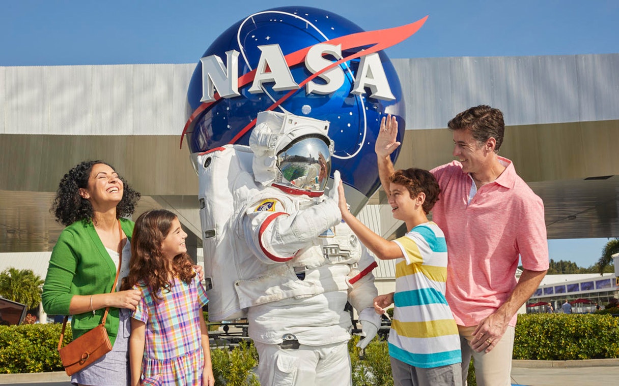 Family with astronaut at Kennedy Space Center, NASA globe in background.
