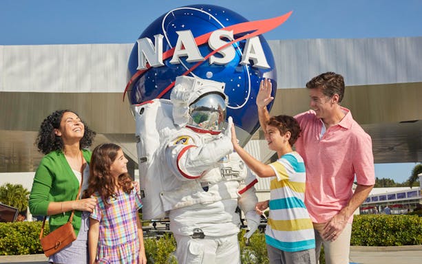 Family with astronaut at Kennedy Space Center, NASA globe in background.