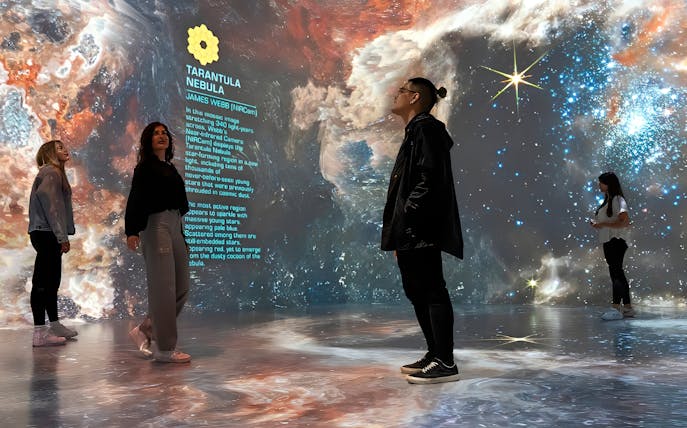Visitors explore a space-themed exhibit with projections of the Tarantula Nebula and James Webb telescope information.