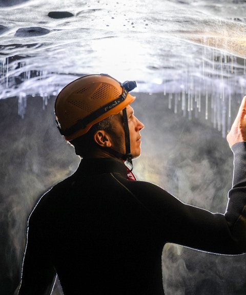 Person exploring Okohua Glowworm Cave, pointing at glowworms on the ceiling.