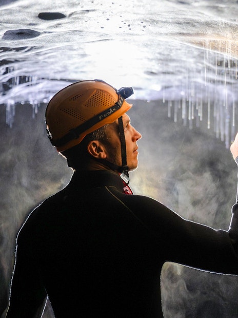 Person exploring Okohua Glowworm Cave, pointing at glowworms on the ceiling.