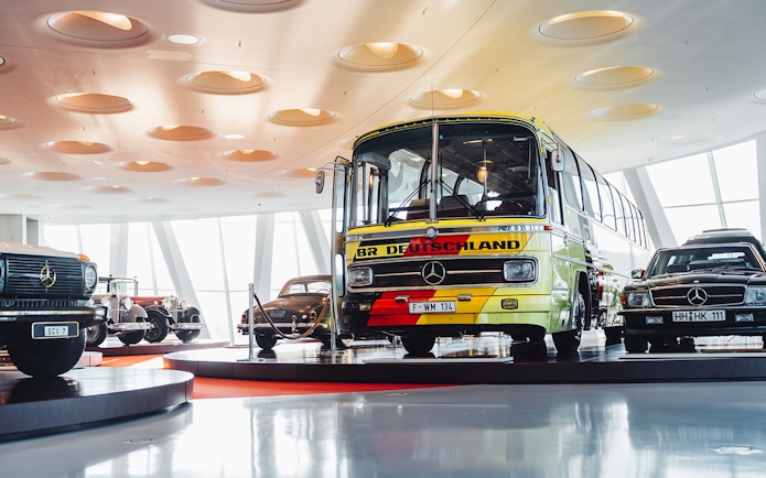 Mercedes Benz touring coach displayed in a museum setting with vintage cars.