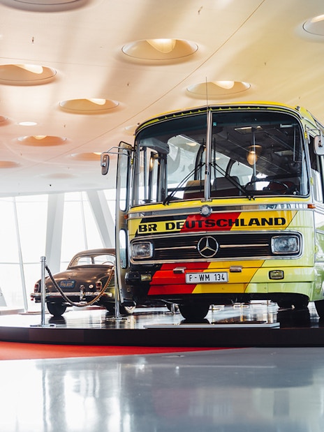 Mercedes Benz touring coach displayed in a museum setting with vintage cars.
