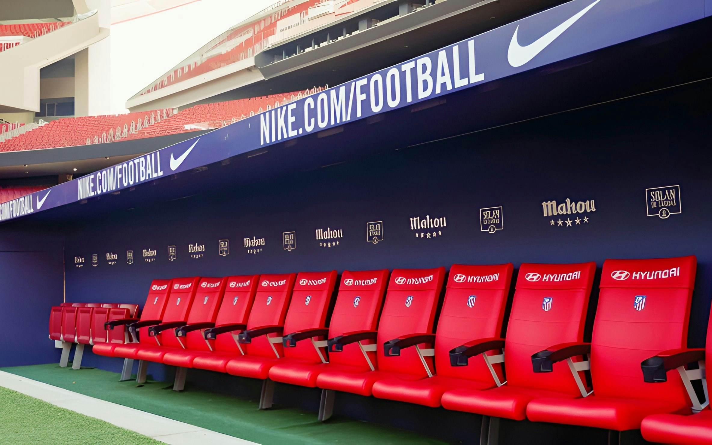 Players seating area at Atletico de Madrid Stadium with red chairs and sponsor logos.