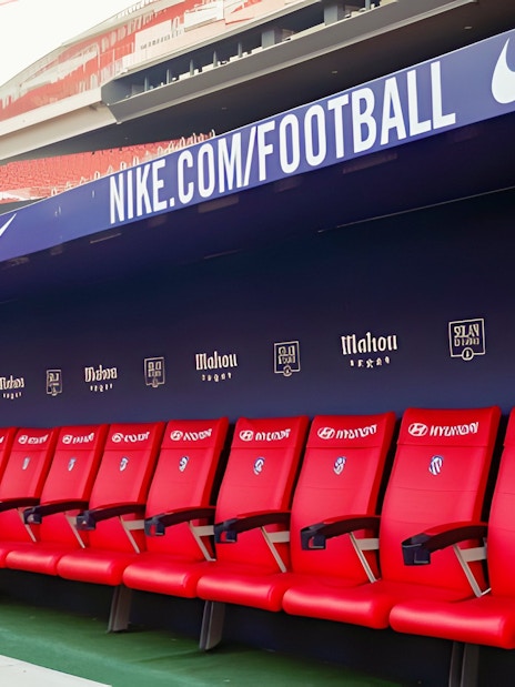 Players seating area at Atletico de Madrid Stadium with red chairs and sponsor logos.