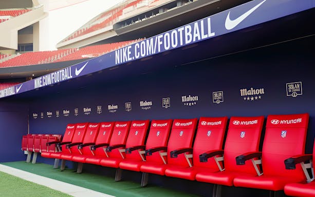 Players seating area at Atletico de Madrid Stadium with red chairs and sponsor logos.