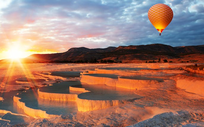 Hot air balloon over Pamukkale travertine terraces at sunrise, Turkey.