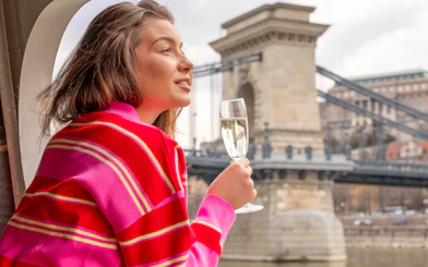 Woman enjoying a drink on Budapest Danube River cruise with Chain Bridge in background.