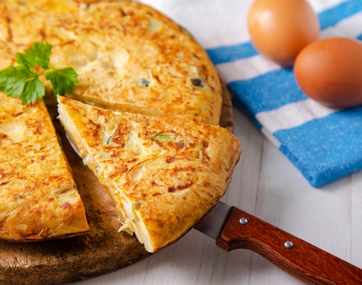 Mushroom omelette with potatoes and zucchini on a wooden board.