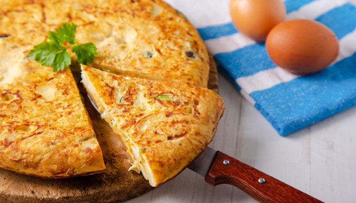Traditional Spanish omelette with potatoes and zucchini on a wooden board.