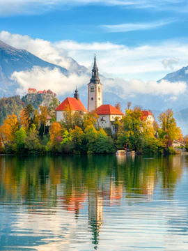 Church on Bled Island with autumn trees and mountains, Lake Bled, Slovenia.
