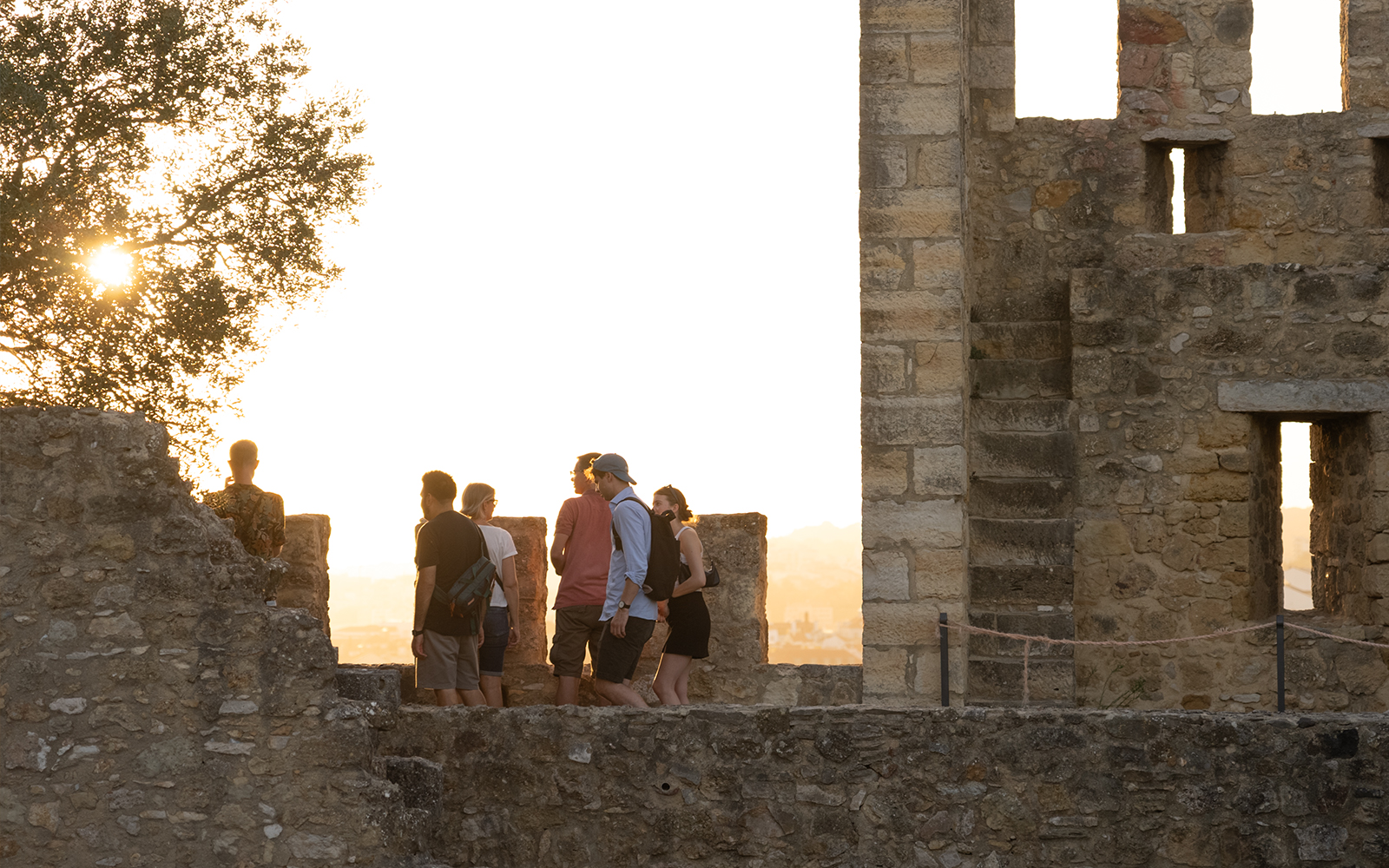 Visitors exploring St. George Castle at sunset, Lisbon, with audio tour on phone.