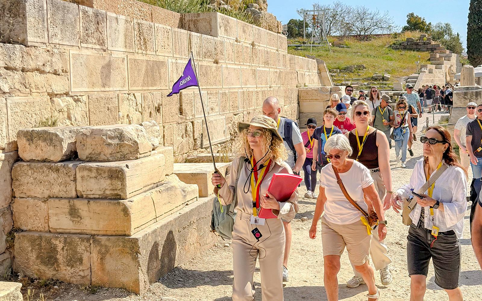 Tour group exploring the Acropolis in Athens with a guide holding a flag.