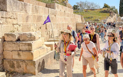 Tour group exploring the Acropolis in Athens with a guide holding a flag.