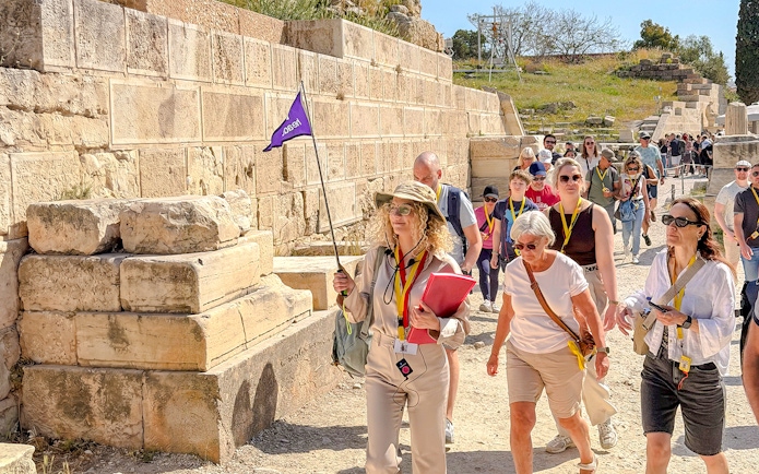 Tour group exploring the Acropolis in Athens with a guide holding a flag.