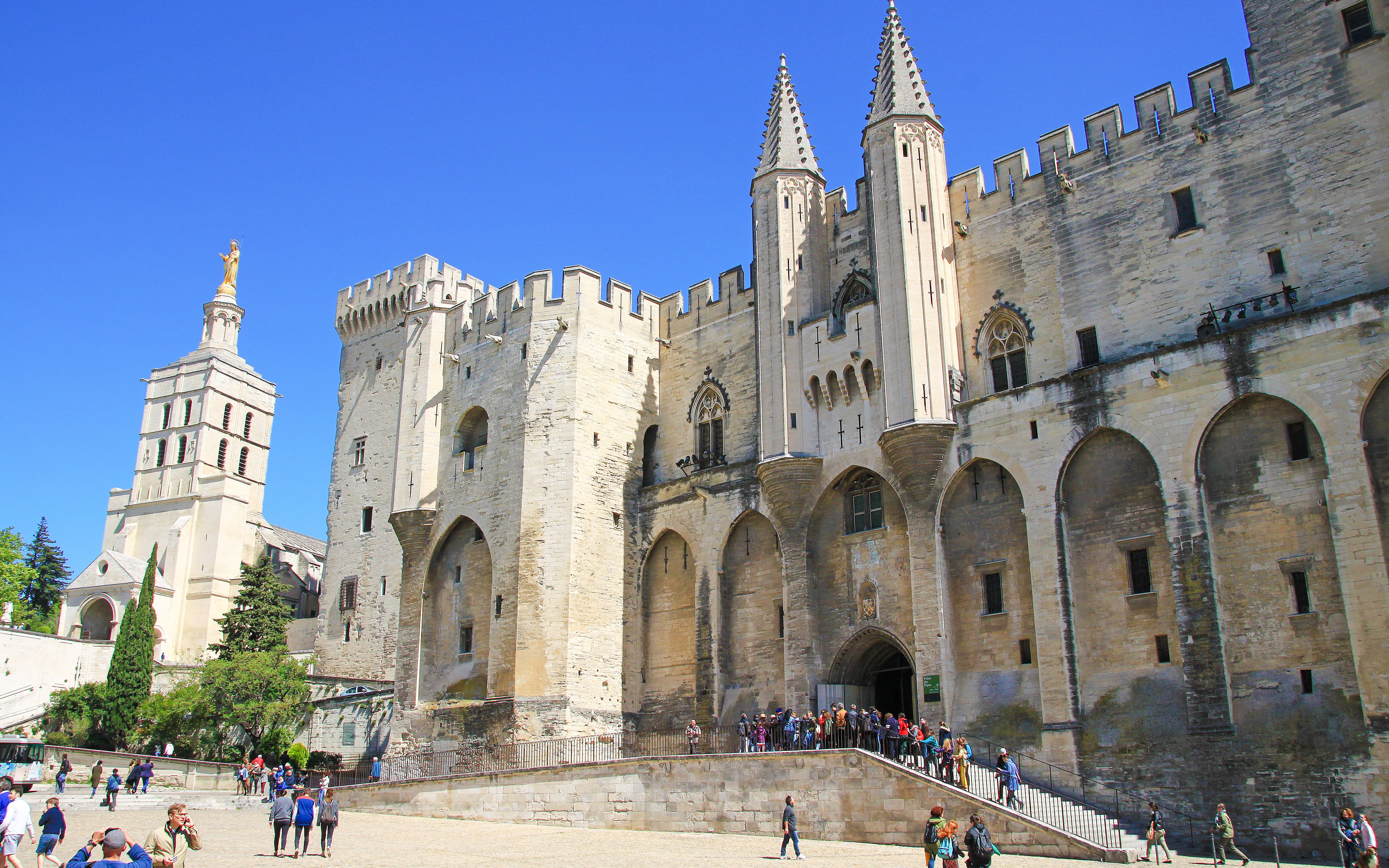 Popes Palace in Avignon with tourists exploring the historic architecture.