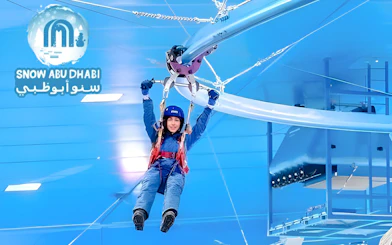 Person ziplining indoors at Snow Abu Dhabi, wearing winter gear.