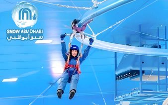 Person ziplining indoors at Snow Abu Dhabi, wearing winter gear.