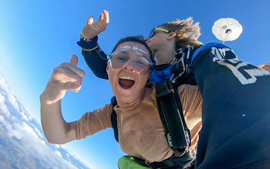 Tandem skydive over Airlie Beach with parachute deployed, clear blue sky.