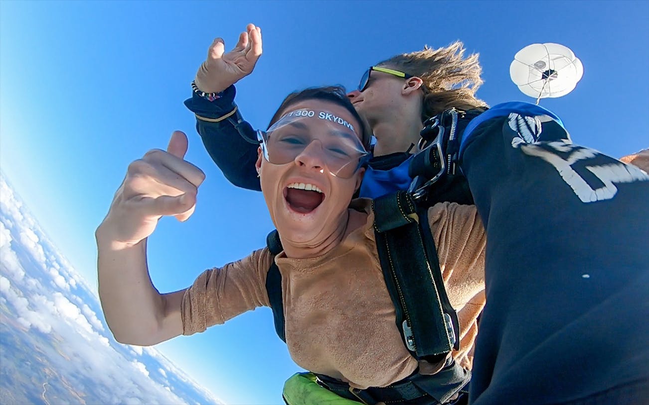 Tandem skydive over Airlie Beach with parachute deployed, clear blue sky.