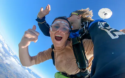 Tandem skydive over Airlie Beach with parachute deployed, clear blue sky.